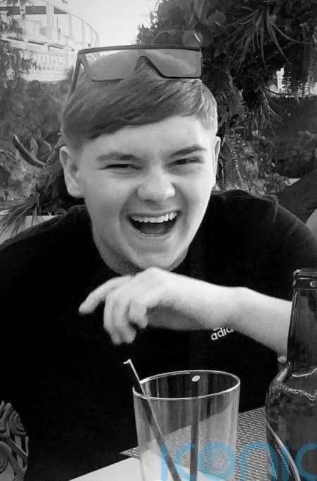 A black and white image of Harvey Willgoose, he's wearing sunglasses on his head and laughing at the camera