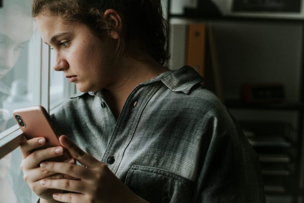 Sad teenager on phone looking out the window