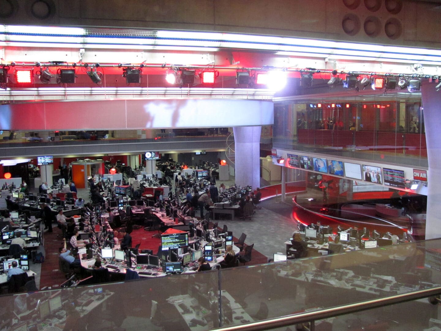A wide view of a BBC newsroom, with red desks and lots of people working at their computers.