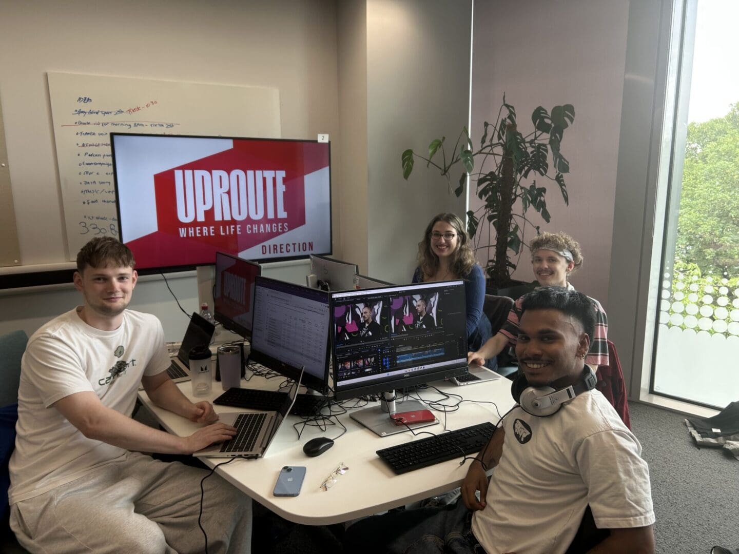 Four members from Uproute magazine sat at desks writing stories. All 4 are smiling at the camera, and there is a larger computer screen with Uproute displayed on it