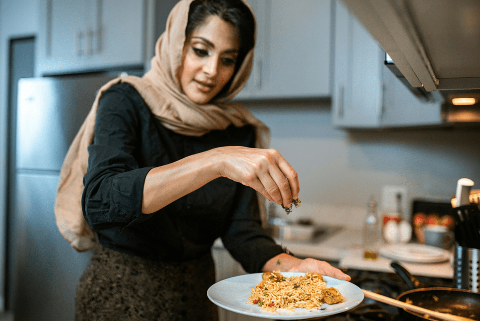 A woman garnishing a plate of food.