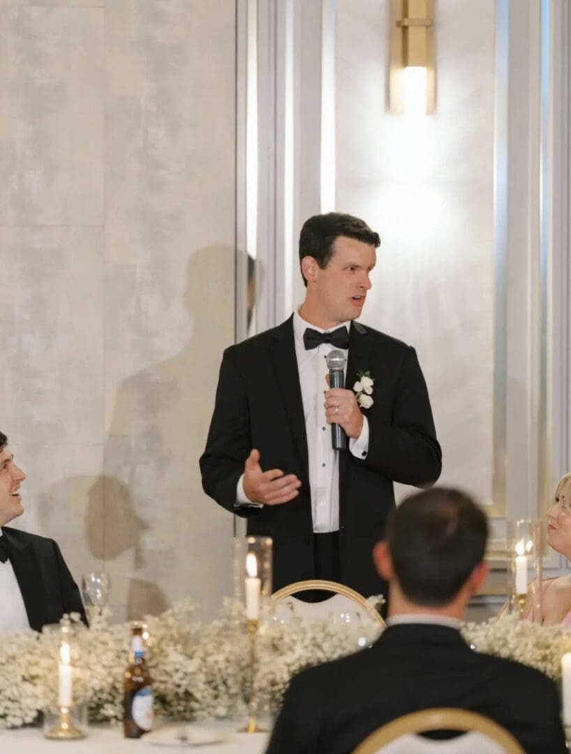 A photo of Wes in a suit and tie giving a speech