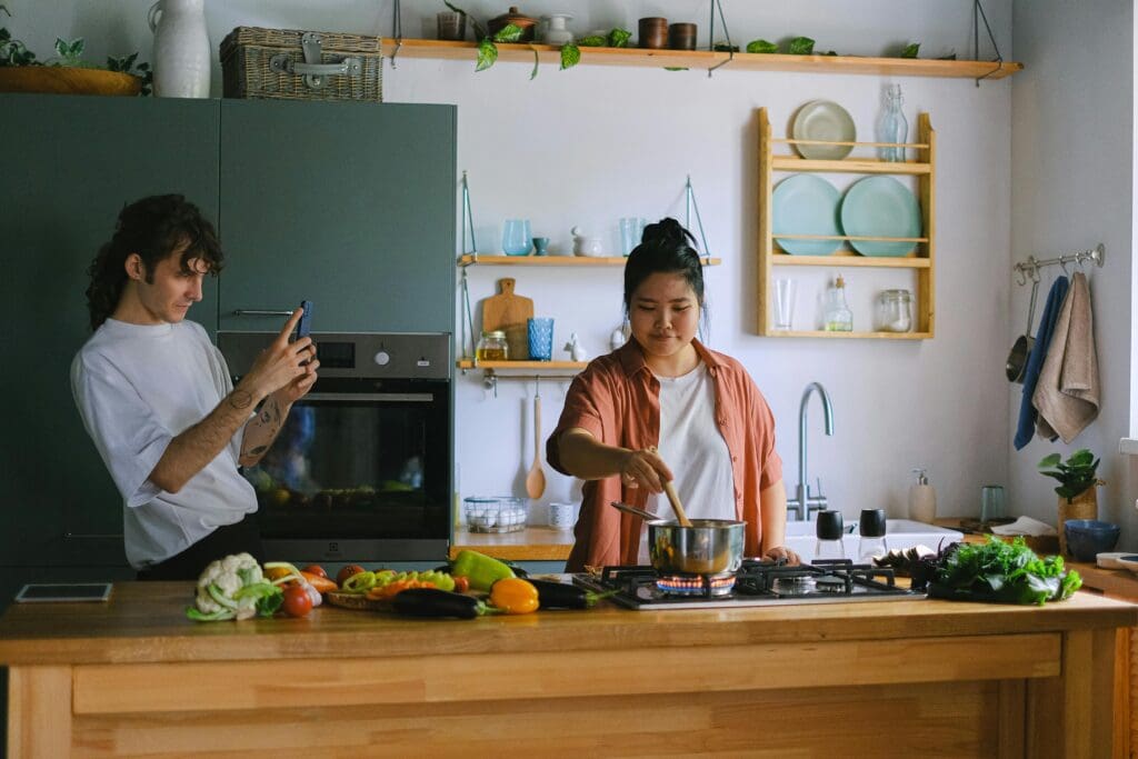 A man clicking a picture of a woman cooking.