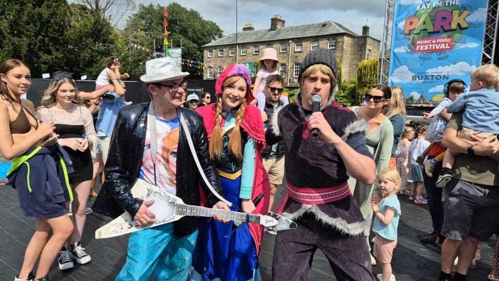 Zach at a festival dressed in a sparkly black jacket and sparkly silver hat playing the guitar. 