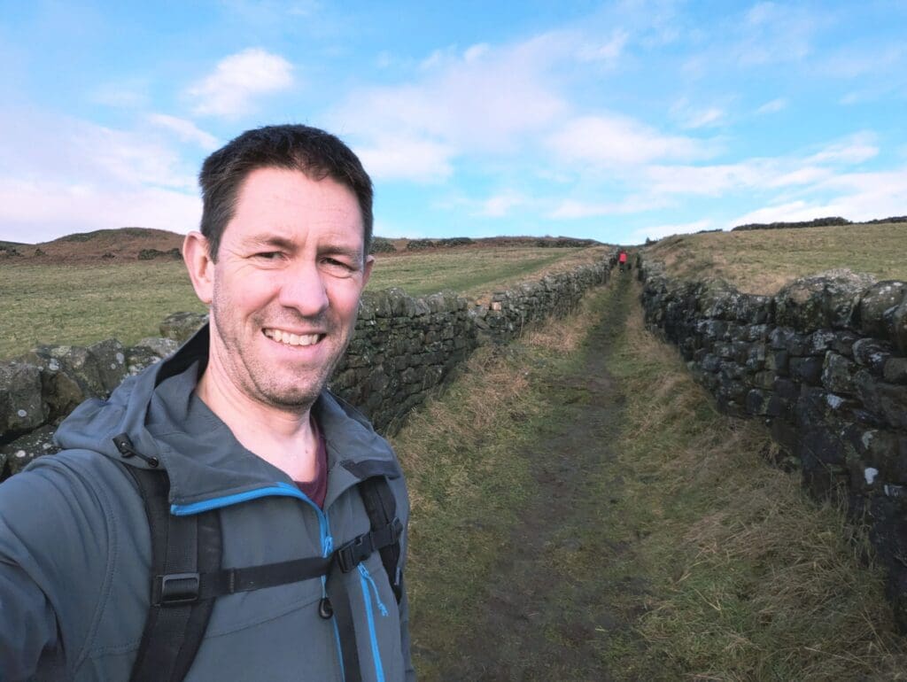 A photo of Steve Hoey facing the camera whilst on a walk between two stone walls in a field