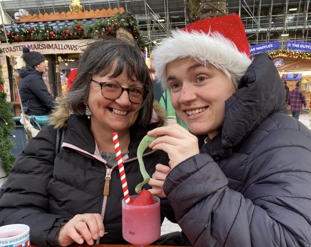 Lee and Jenny at the Christmas markets sharing a frozen strawberry drink. Jenny is wearing a red and white Christmas Santa hat.