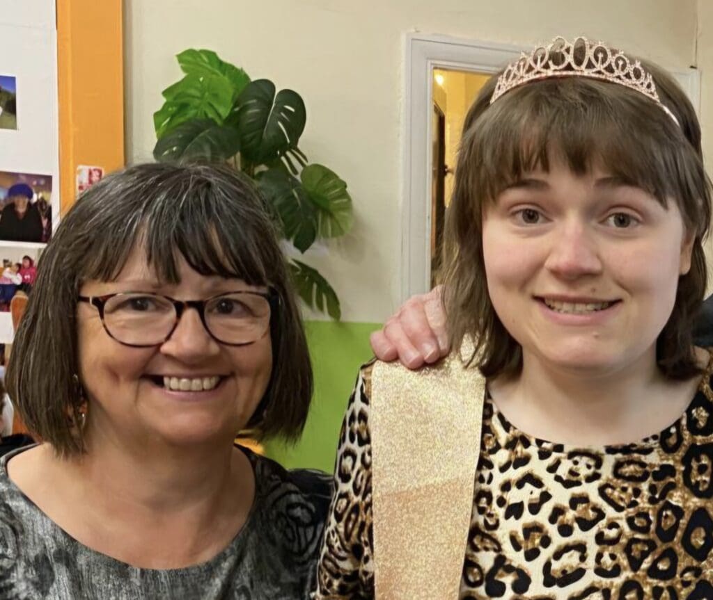 Lee, on the left has short hair and is wearing glasses. Jenny is stood next to her, wearing a 30th birthday crown and a gold leopard print dress